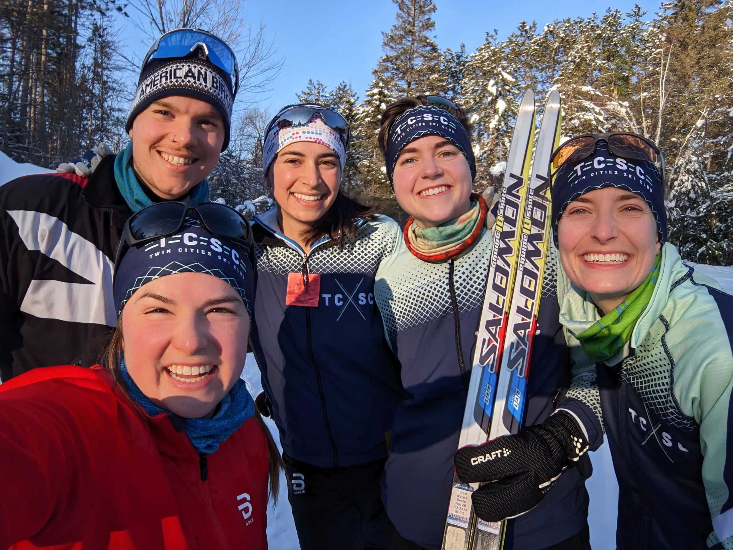Five members in club kits shoulder to shoulder on a snowy trail in low winter sun